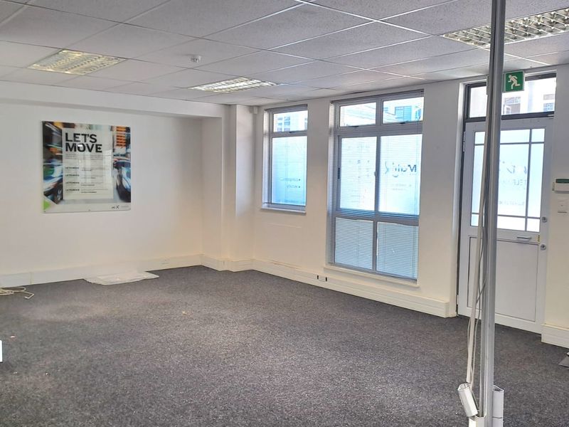 A vacant office space featuring a suspended ceiling, recessed lighting, carpeted flooring, and large windows providing natural light.
