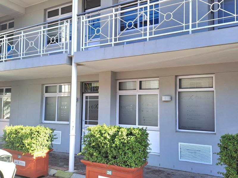 Front elevation of a two-story office building featuring a paved entrance area, balconies with metal railings, and large windows with frosted privacy film.