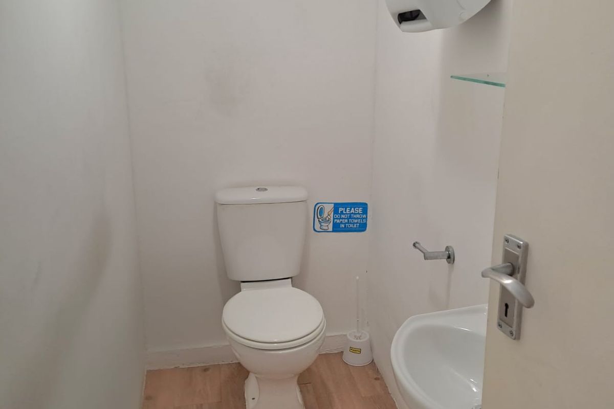 A compact office restroom featuring a standard toilet, wall-mounted basin, and laminate flooring.