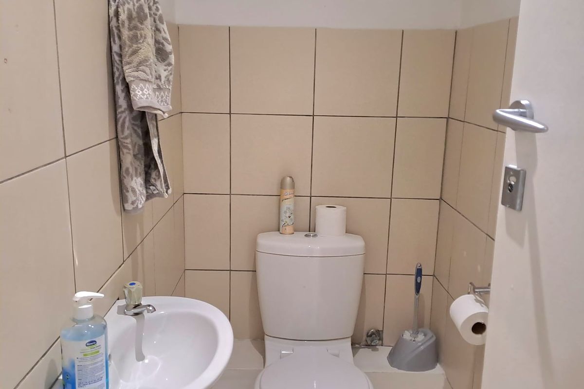 A compact office restroom featuring a wall-mounted basin and a standard white toilet with neutral wall tiling.