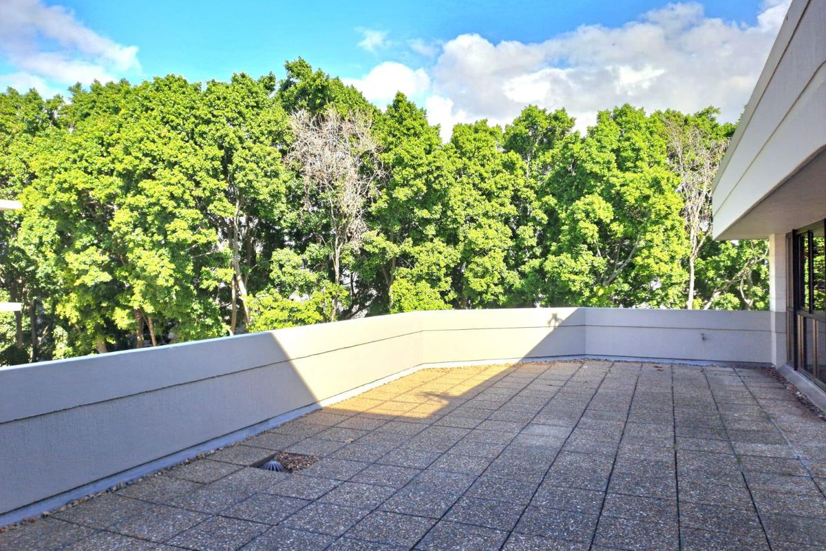 A spacious outdoor balcony featuring concrete paving, a solid parapet wall, and a pleasant outlook towards mature trees.