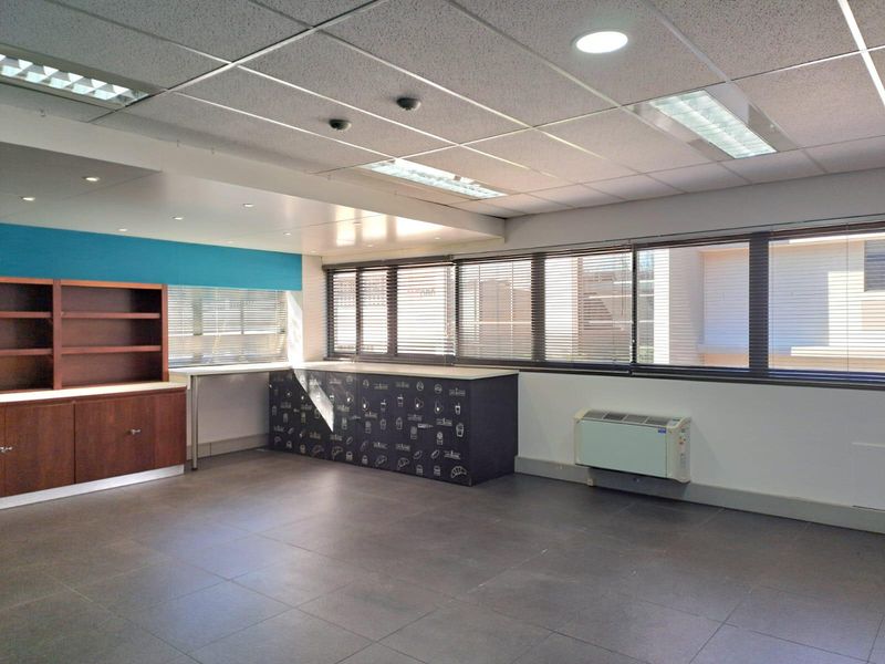 A bright, open-plan office space featuring tiled flooring, suspended ceilings with recessed lighting, built-in cabinetry, and integrated HVAC climate control.
