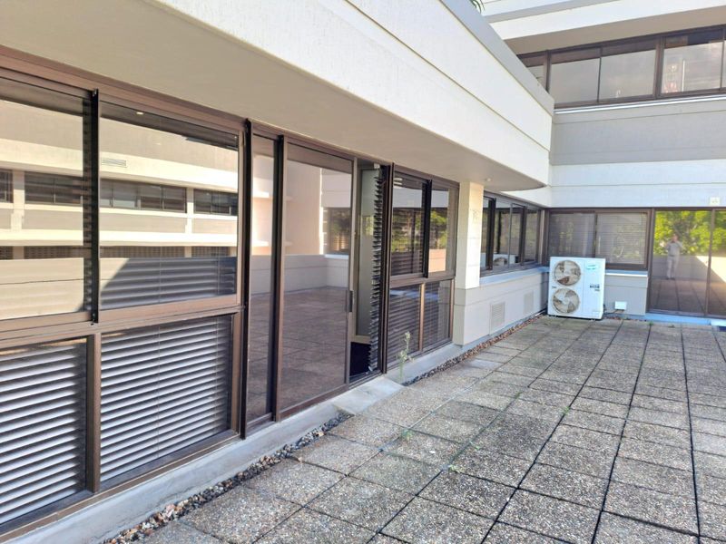 A spacious paved balcony area featuring sliding glass doors and an external air conditioning unit, providing outdoor access for the office suite.