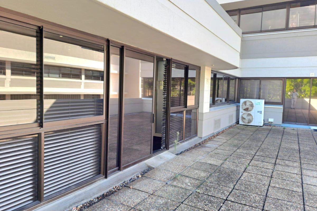 A spacious paved balcony area featuring sliding glass doors and an external air conditioning unit, providing outdoor access for the office suite.