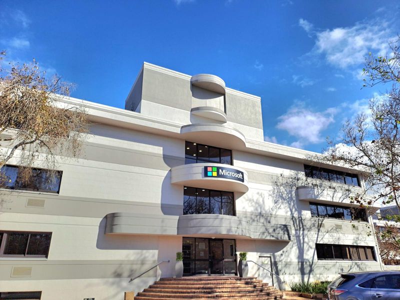 A well-maintained multi-story office building facade featuring modern curved architectural elements, brick entrance steps, and prominent corporate signage.