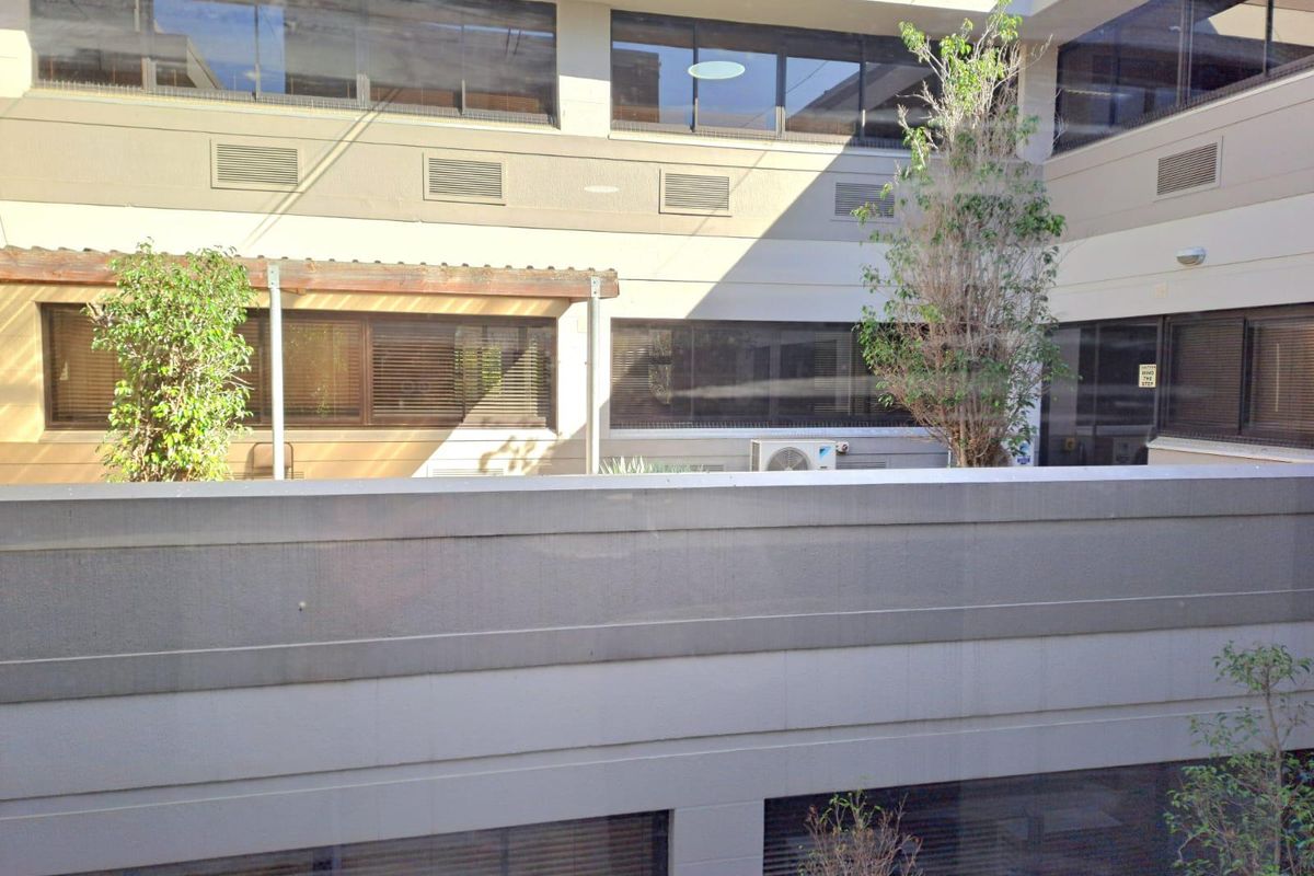 View of the office building exterior courtyard featuring multi-level windows, HVAC infrastructure, and a pergola structure.