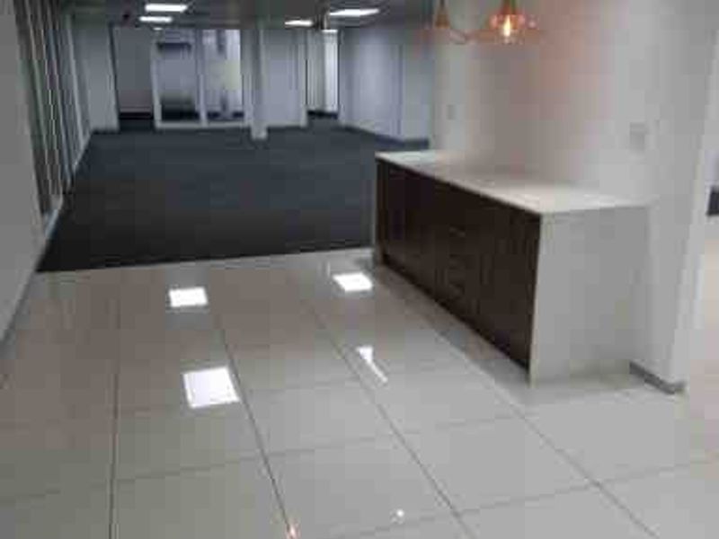 A spacious open-plan commercial office area featuring a mix of tiled and carpeted flooring, built-in cabinetry, and modern recessed ceiling lighting.