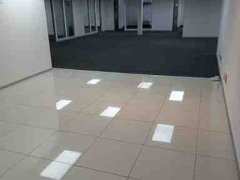 A spacious, vacant open-plan commercial office area featuring a combination of polished tile and carpet flooring with modern recessed ceiling lighting.