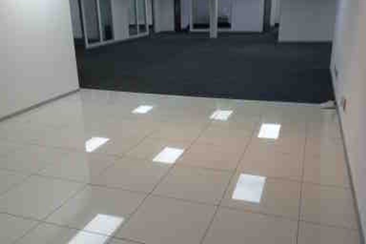 A spacious, vacant open-plan commercial office area featuring a combination of polished tile and carpet flooring with modern recessed ceiling lighting.
