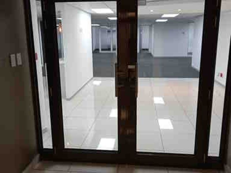 A bright, modern commercial entrance featuring double glass doors, polished tiled flooring, and a clean, open-plan office space visible beyond.