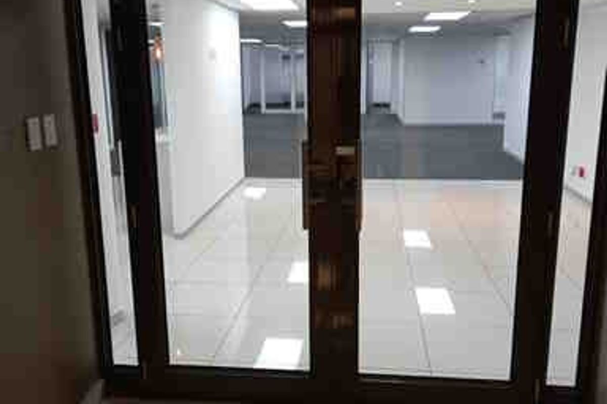 A bright, modern commercial entrance featuring double glass doors, polished tiled flooring, and a clean, open-plan office space visible beyond.