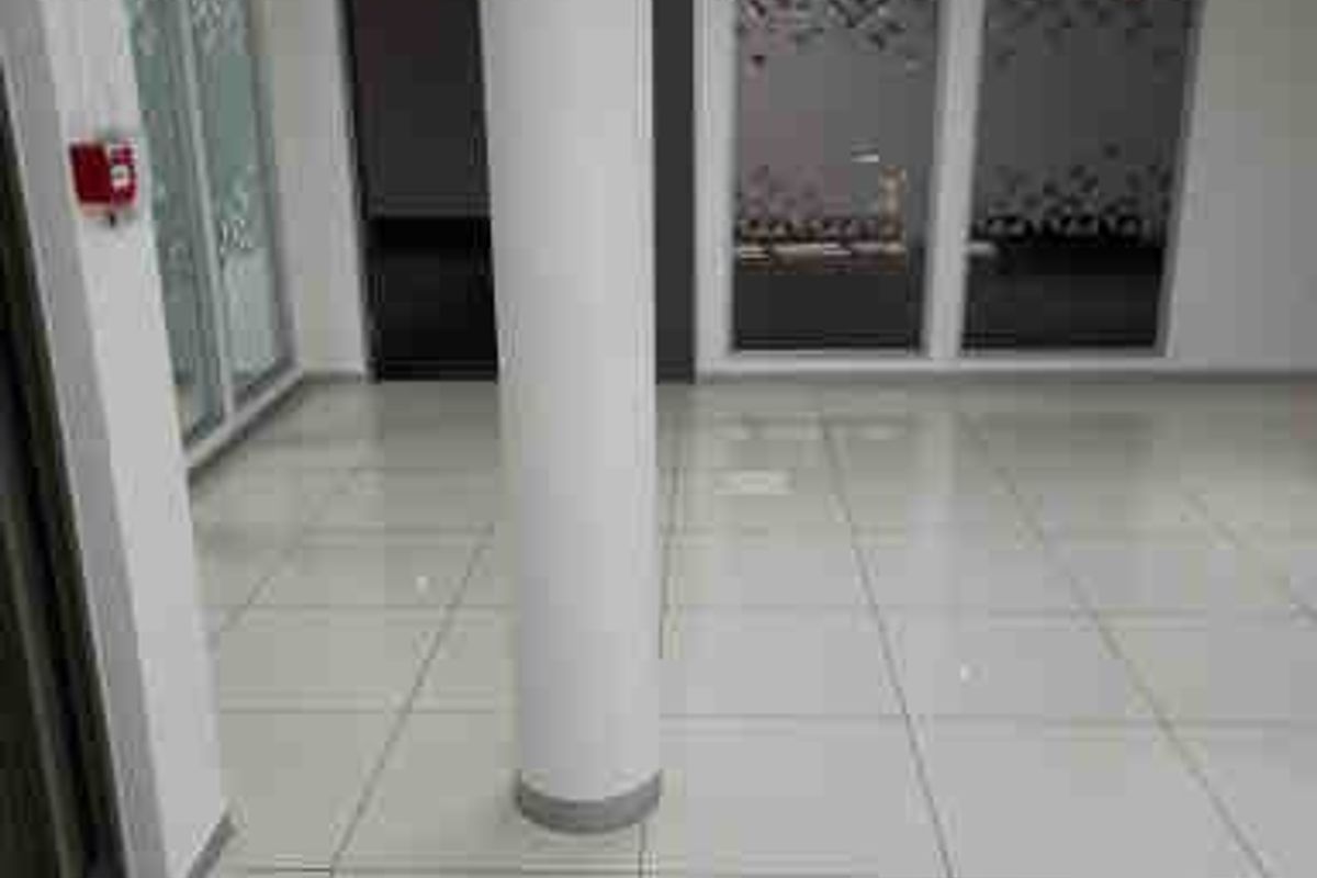 A bright, vacant commercial office space featuring polished porcelain tile flooring, a central structural column, and modern glass partition walls.