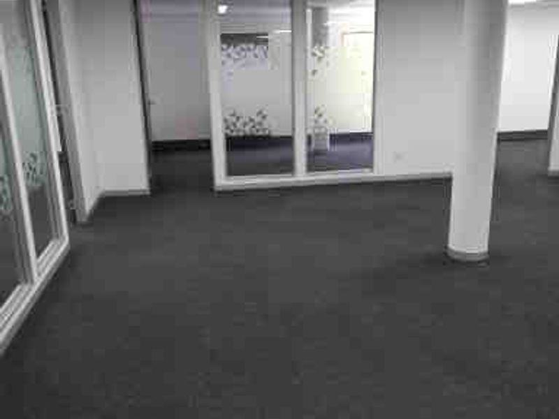 An open-plan commercial office space featuring glass partitions, carpeted flooring, and a suspended ceiling with recessed lighting.