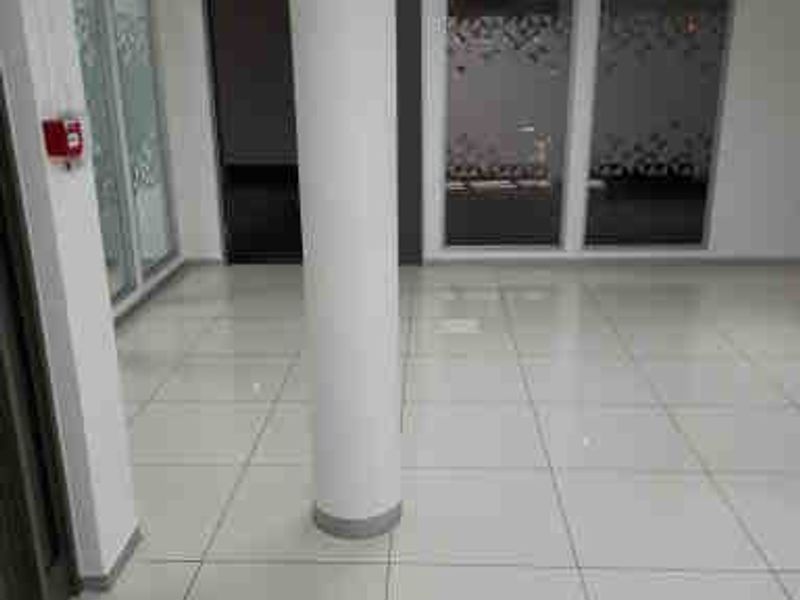 A bright, vacant commercial office space featuring polished porcelain tile flooring, a central structural column, and modern glass partition walls.