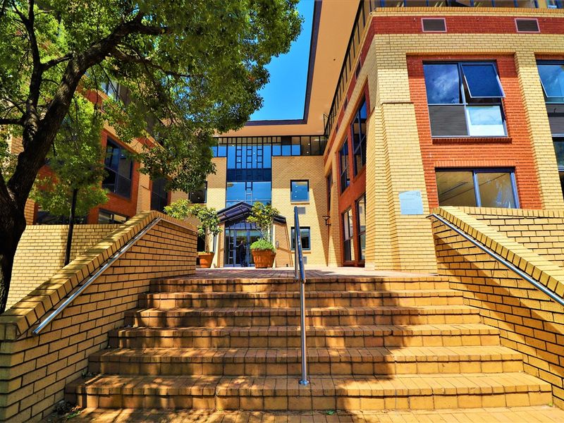 Front entrance of a multi-story office building featuring a brick facade, wide brick staircase with stainless steel handrails, and a glass entrance canopy.