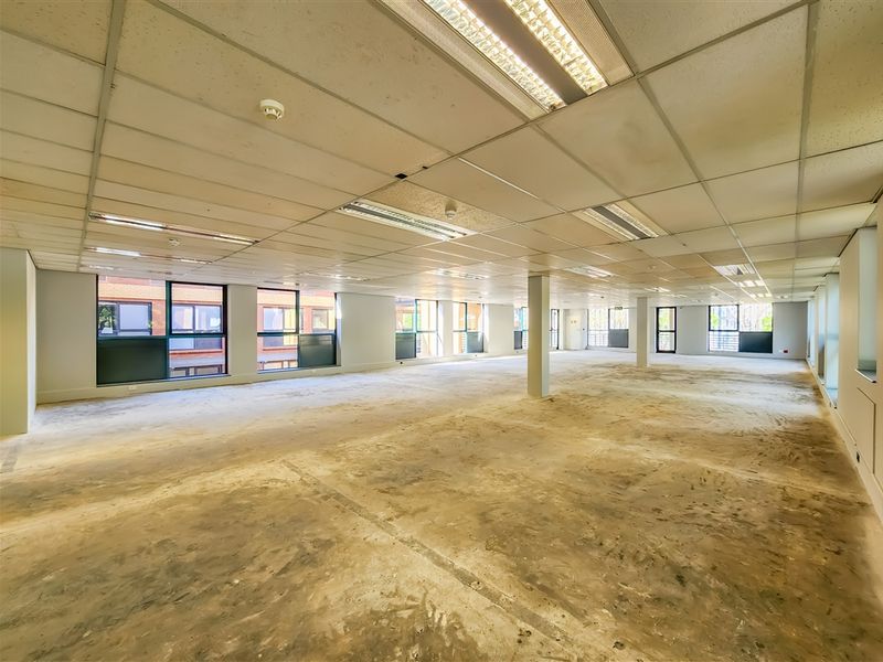 A large, open-plan office space featuring a suspended ceiling, structural columns, and expansive windows, currently in a shell condition ready for fit-out.
