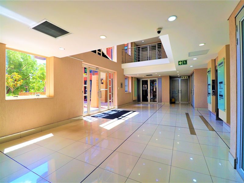 Spacious and modern office building lobby featuring polished tiled floors, recessed lighting, and a bright, open-plan atrium design with secure glass entryways.