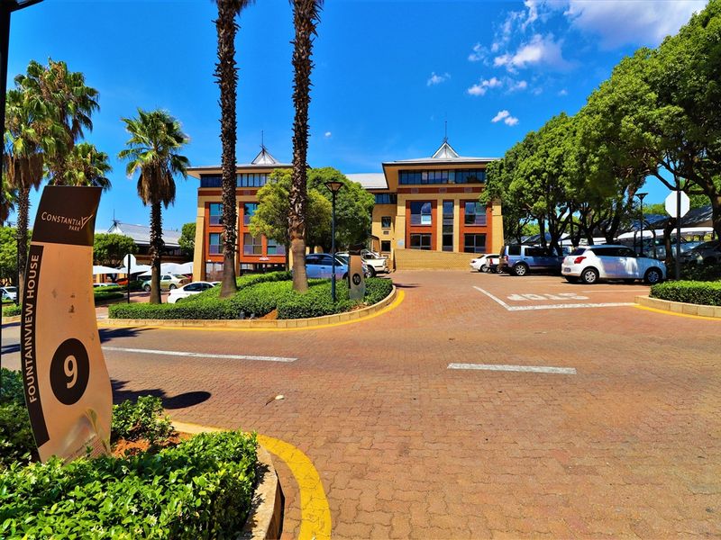 Front view of Fountainview House office building featuring a paved driveway, landscaped gardens, and ample parking space.