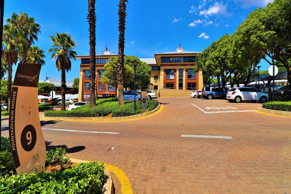 Front view of Fountainview House office building featuring a paved driveway, landscaped gardens, and ample parking space.