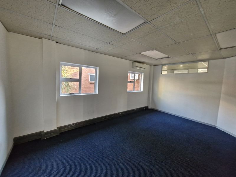 A vacant office space featuring a suspended ceiling, recessed lighting, split-system air conditioning, and blue carpeted flooring.
