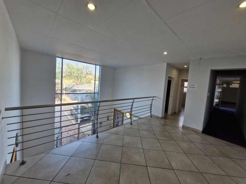 Spacious office hallway featuring tiled flooring, a modern stainless steel balustrade, and large windows providing natural light and views of the exterior.