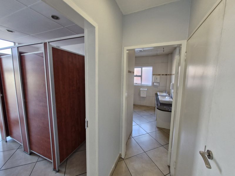 A functional office bathroom facility featuring multiple toilet cubicles and a vanity area with double basins and tiled flooring.