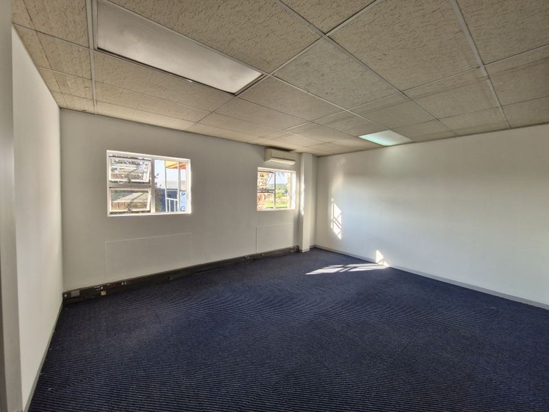 A vacant office space featuring a suspended ceiling, recessed lighting, wall-mounted air conditioning, and carpeted flooring with perimeter trunking for connectivity.