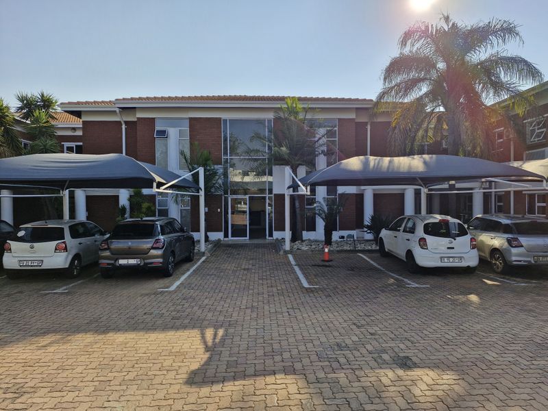 Front exterior view of a professional office building featuring a brick facade, glass entrance, and dedicated paved parking with shade cloth carports.