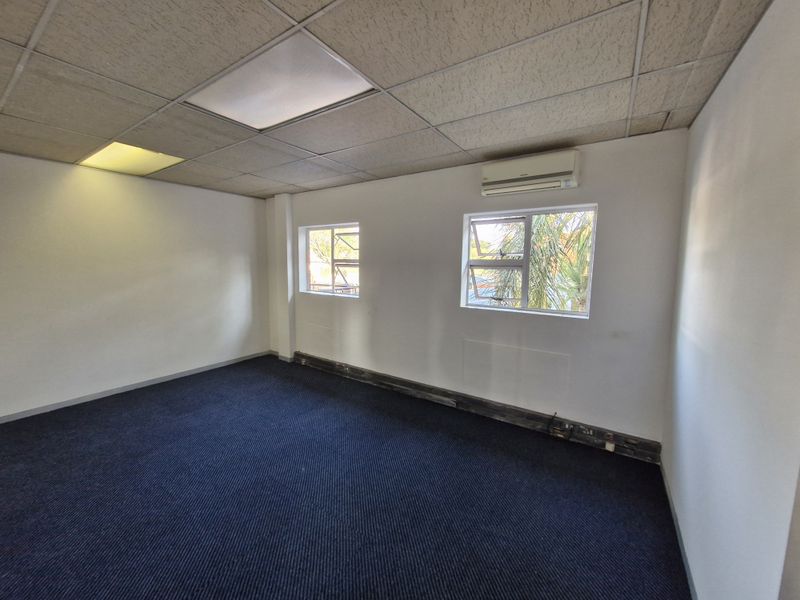 A vacant office space featuring a suspended ceiling, recessed lighting, split-system air conditioning, and blue carpet flooring.