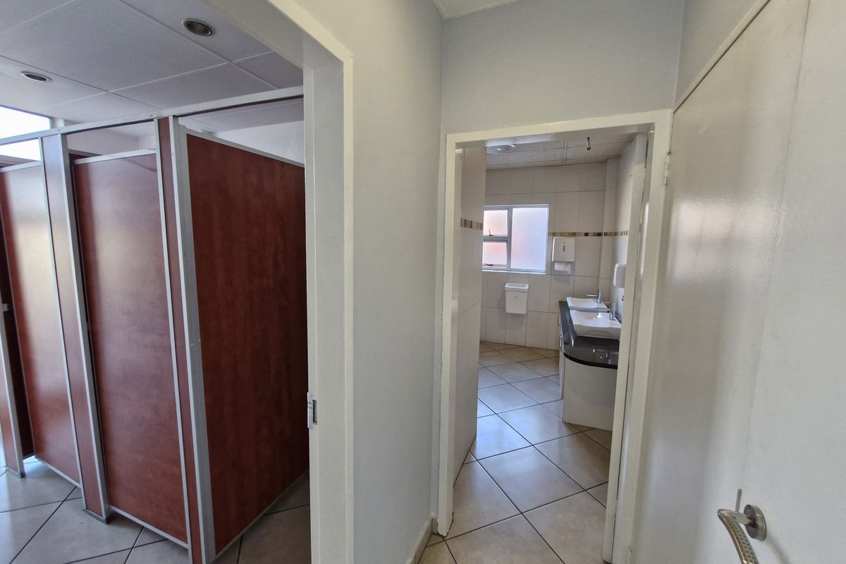 A functional office bathroom facility featuring multiple toilet cubicles and a vanity area with double basins and tiled flooring.