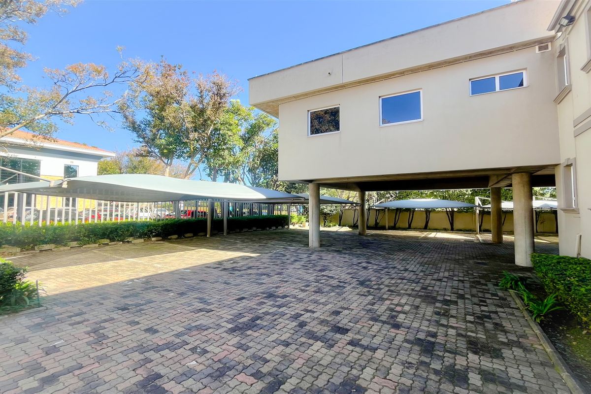 Exterior view of the office property featuring a paved parking area with covered shade-cloth carports and landscaped garden borders.