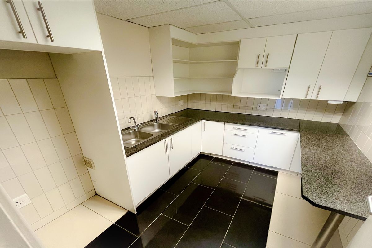 A functional office kitchenette featuring white cabinetry, dark granite countertops, a double stainless steel sink, and tiled flooring.