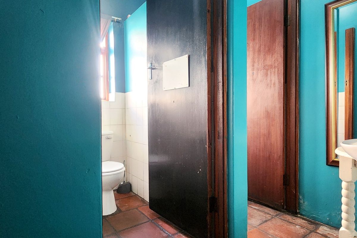 A functional bathroom area featuring tiled flooring, a wall-mounted basin, and a separate toilet cubicle, requiring cosmetic updates to the wall finishes.