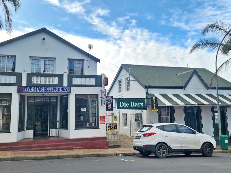 Street-level view of a commercial property featuring two adjacent buildings with storefront signage, security gates, and an awning.
