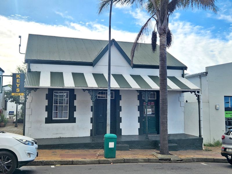 Street-facing commercial property facade featuring a corrugated metal roof, striped awning, and traditional architectural detailing.