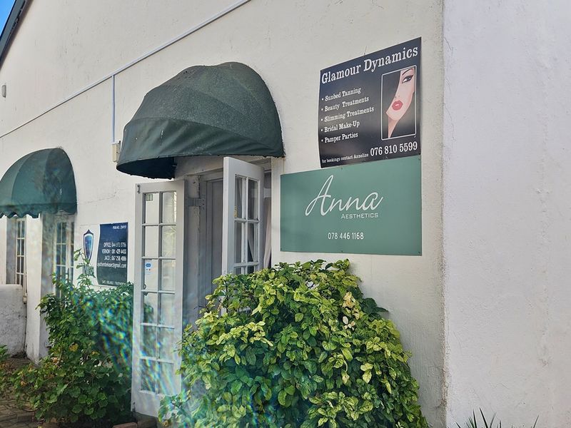 Commercial storefront entrance featuring green fabric awnings, white french doors, and paved courtyard access, currently utilized for beauty and aesthetic services.