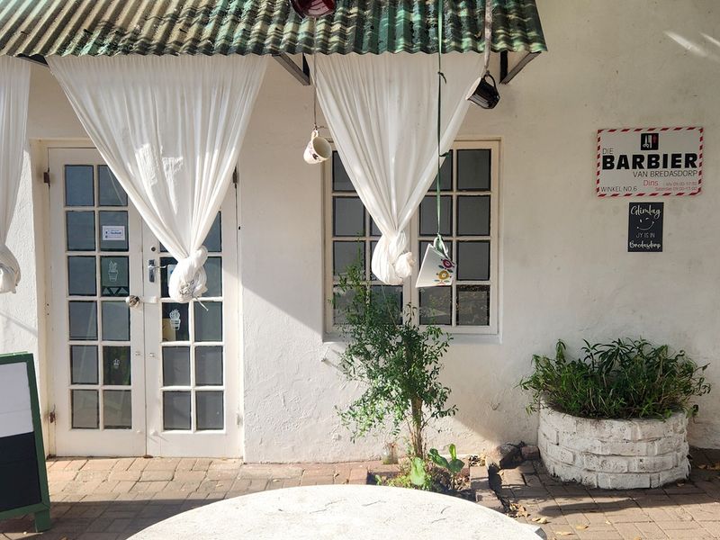 Front entrance of a commercial property featuring a corrugated metal awning, white painted masonry walls, and classic multi-pane french doors.