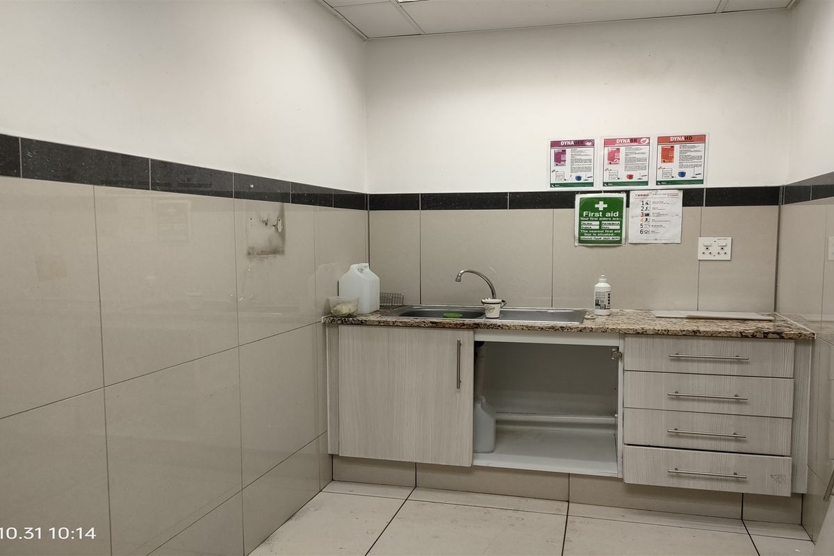 A functional industrial kitchenette area featuring tiled walls, granite countertop, stainless steel sink, and built-in cabinetry.