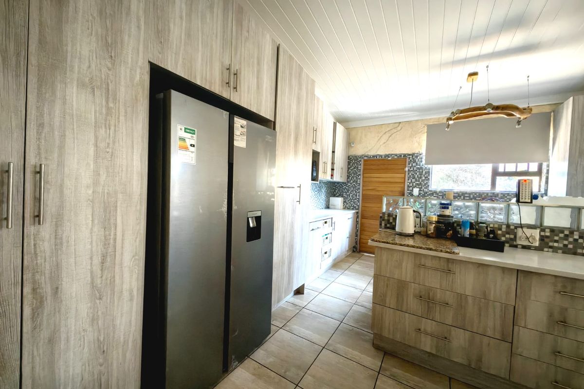 A functional kitchen featuring wood-look cabinetry, granite countertops, mosaic tile backsplash, and tiled flooring with a unique glass block partition.