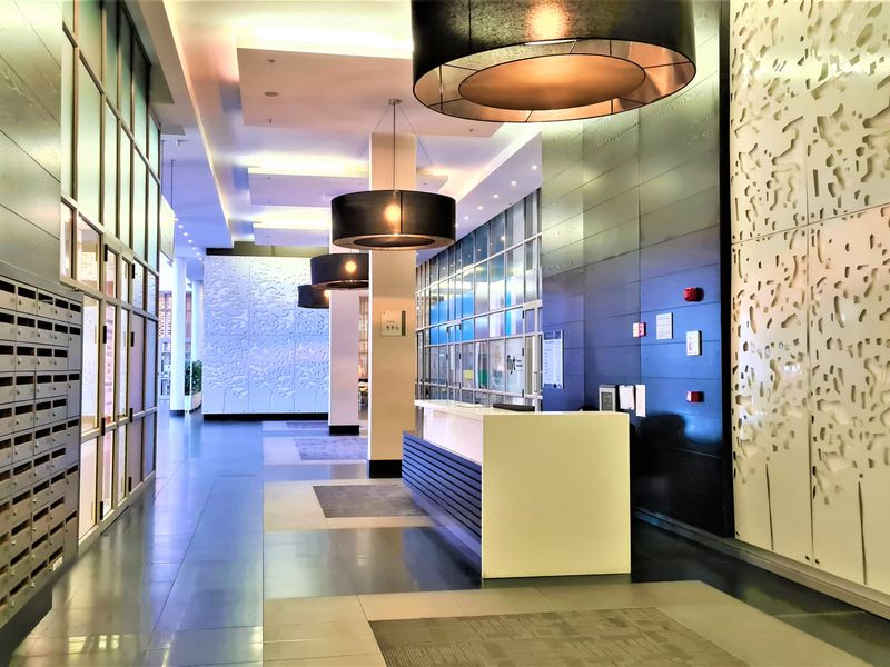 Modern office lobby featuring a reception desk, integrated mailboxes, decorative wall paneling, and contemporary pendant lighting in a professional commercial setting.