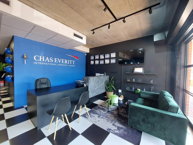 Modern office reception area featuring a bold blue accent wall, exposed concrete ceiling with track lighting, and a professional marble-look reception desk.