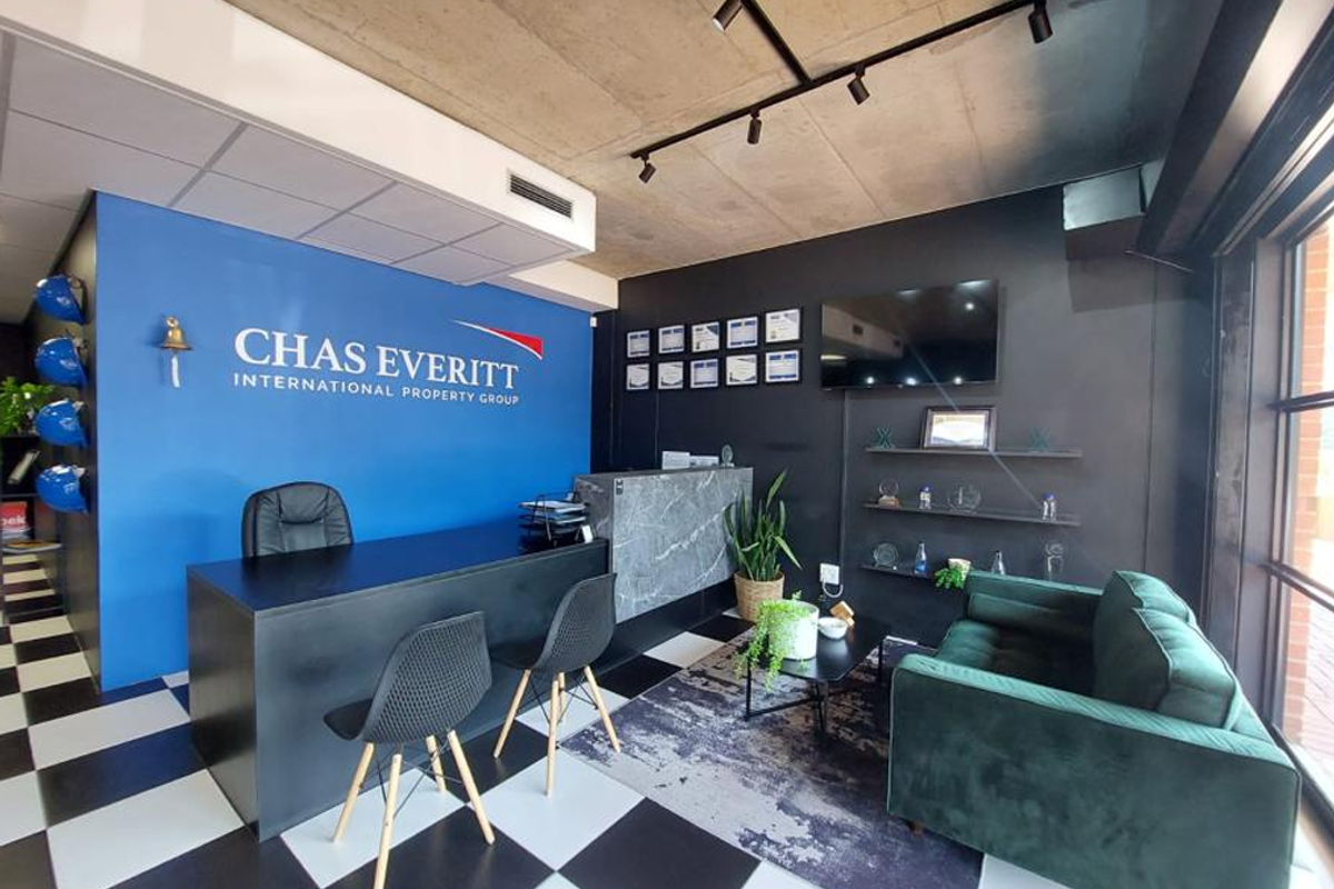 Modern office reception area featuring a bold blue accent wall, exposed concrete ceiling with track lighting, and a professional marble-look reception desk.