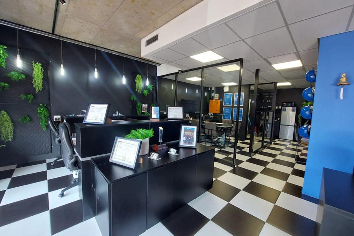 Modern office space featuring a checkerboard floor, exposed concrete ceiling, glass-partitioned meeting area, and contemporary black cabinetry.