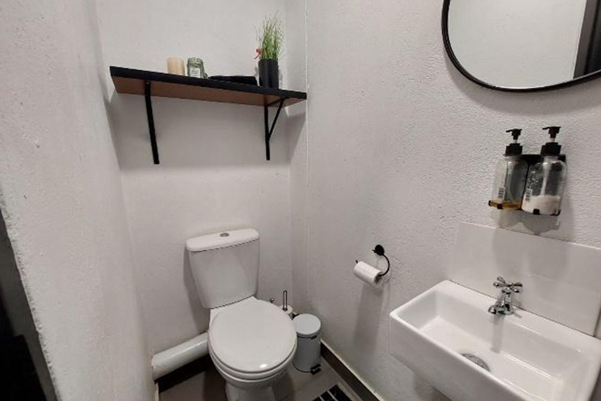 A compact, functional office restroom featuring a wall-mounted basin, modern toilet, and a floating shelf for storage.