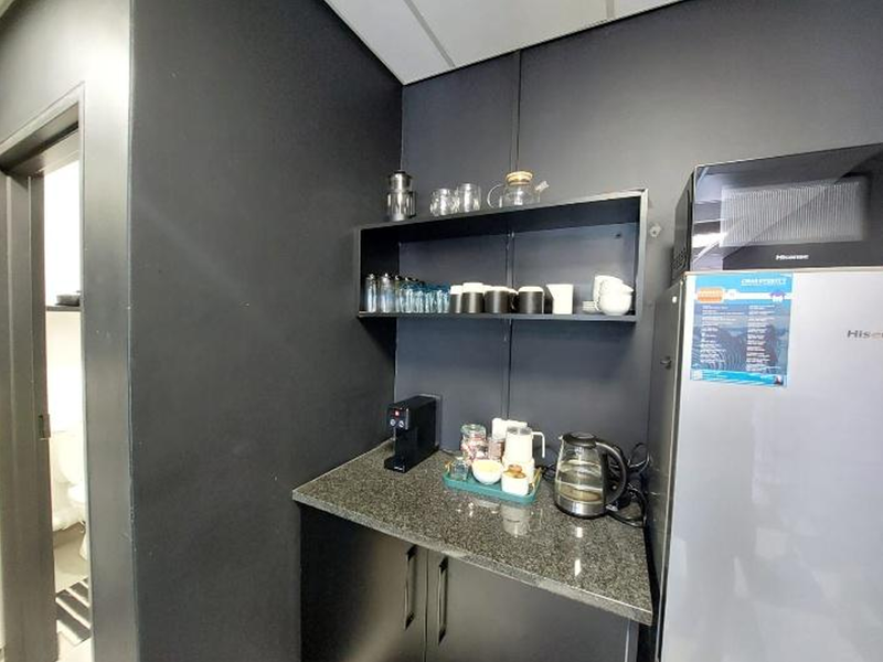 A compact office kitchenette featuring dark cabinetry, granite countertops, and open shelving, providing a functional space for staff refreshments.