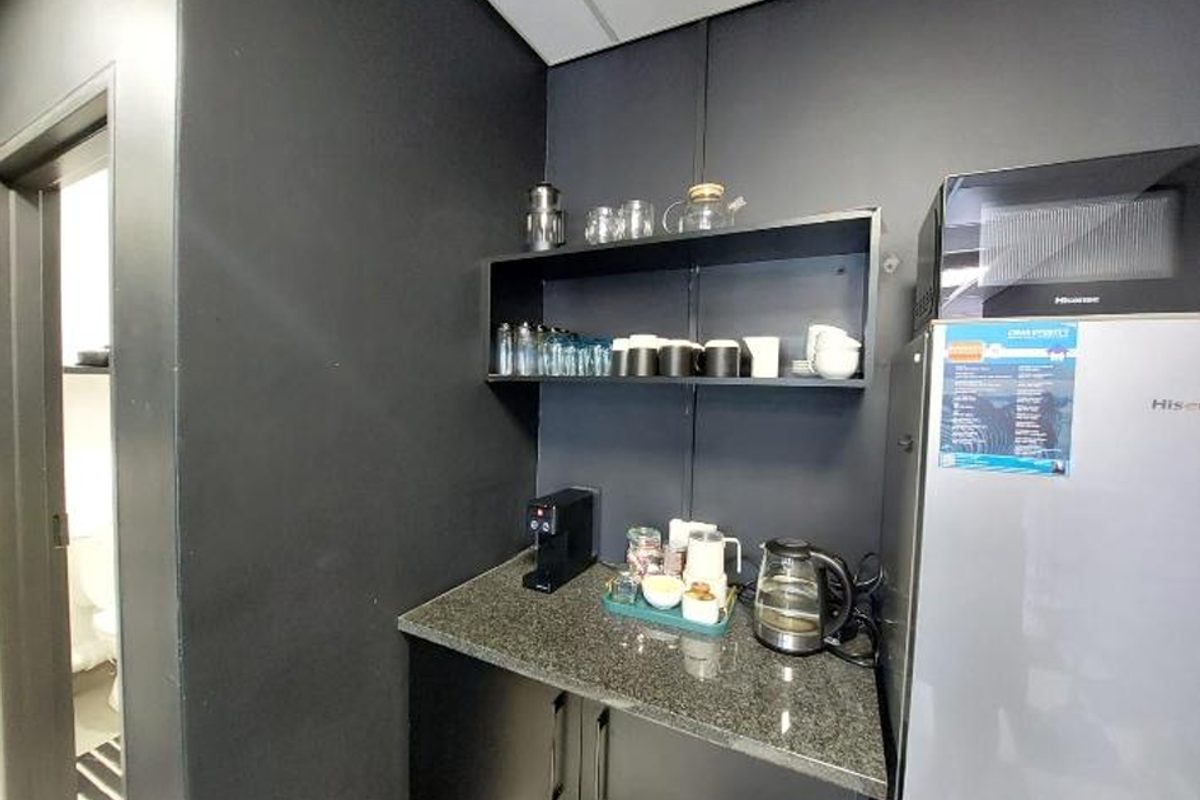 A compact office kitchenette featuring dark cabinetry, granite countertops, and open shelving, providing a functional space for staff refreshments.
