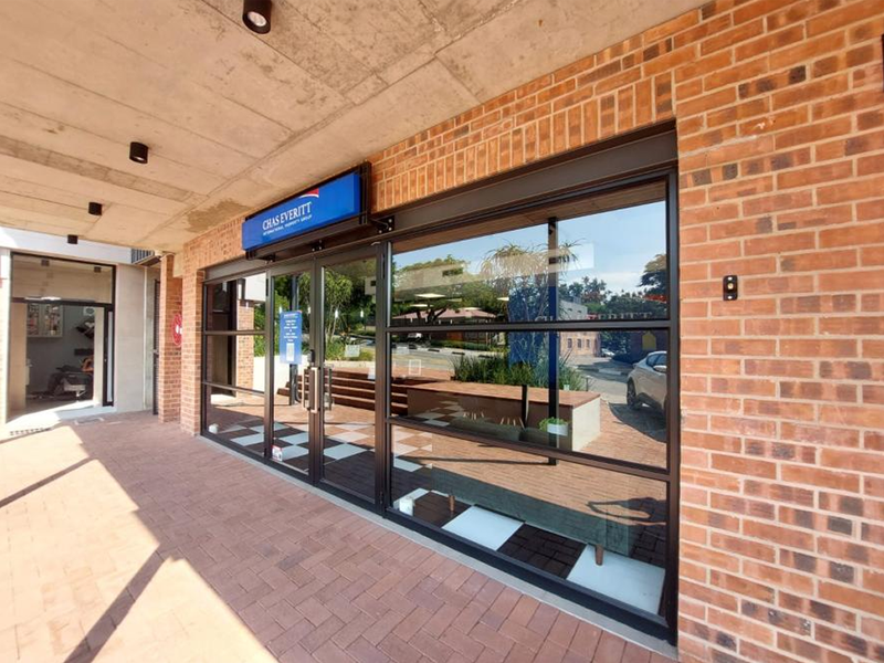 Modern office storefront featuring a brick facade, large glass display windows, and a covered walkway entrance.