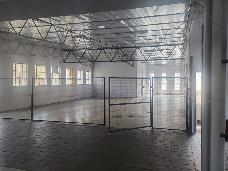 Spacious industrial utility area featuring exposed steel roof trusses, tiled flooring, and secure metal partitioning, suitable for various commercial or storage applications.