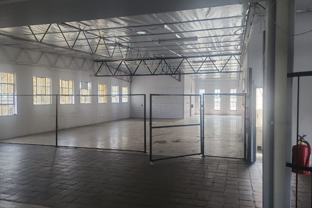 Spacious industrial utility area featuring exposed steel roof trusses, tiled flooring, and secure metal partitioning, suitable for various commercial or storage applications.