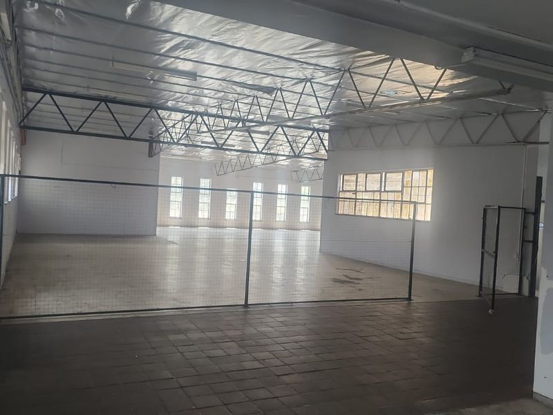 Spacious industrial utility area featuring exposed steel roof trusses, tiled flooring, and large windows, offering a versatile open-plan layout for various commercial uses.